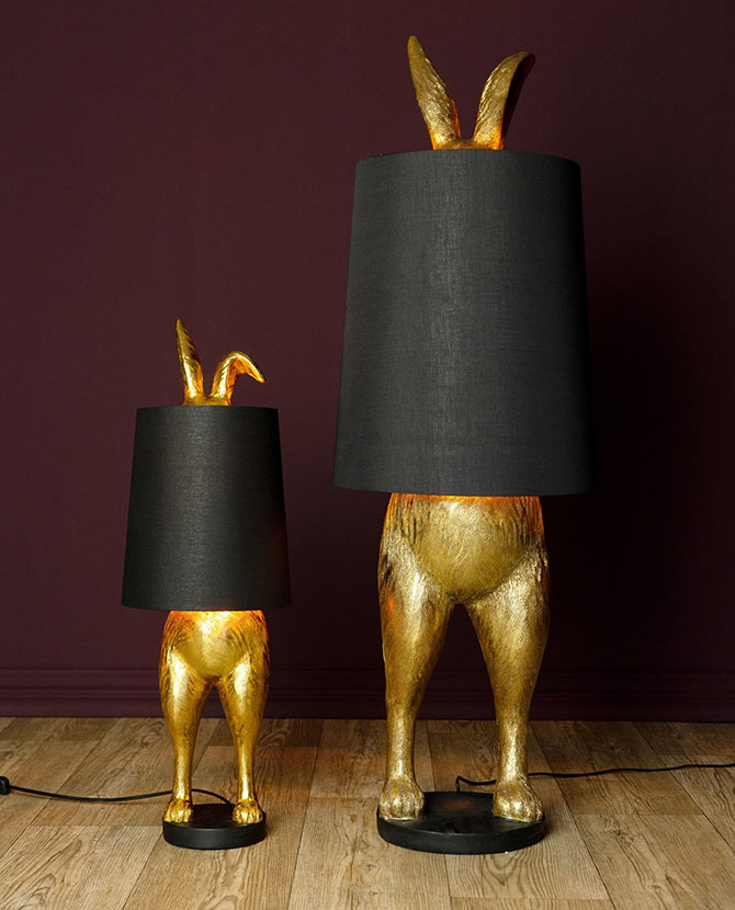 Aranyszínű, rejtőzködő nyuszi figurás, díjnyertes dizájn állólámpa, feketeszínű lámpaernyővel, bordó fal előtt.