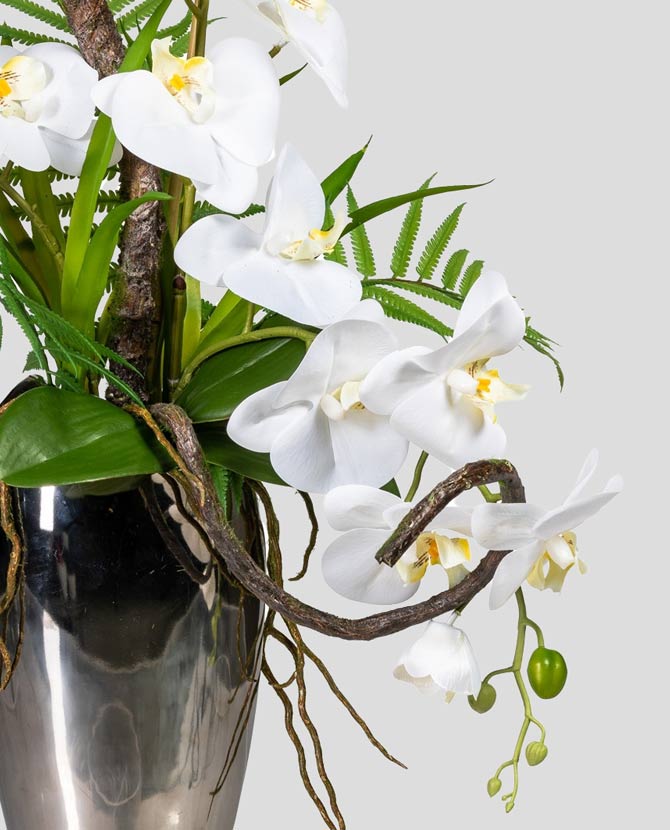 Fehér színű mű orchidea kompozíció, ezüst színű fém vázában.