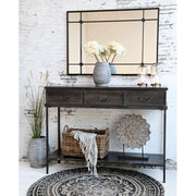 Loft stílusú, fekete falitükör fehérre festett téglafalon, alatta szürkeszínű ipari konzolasztallal. 