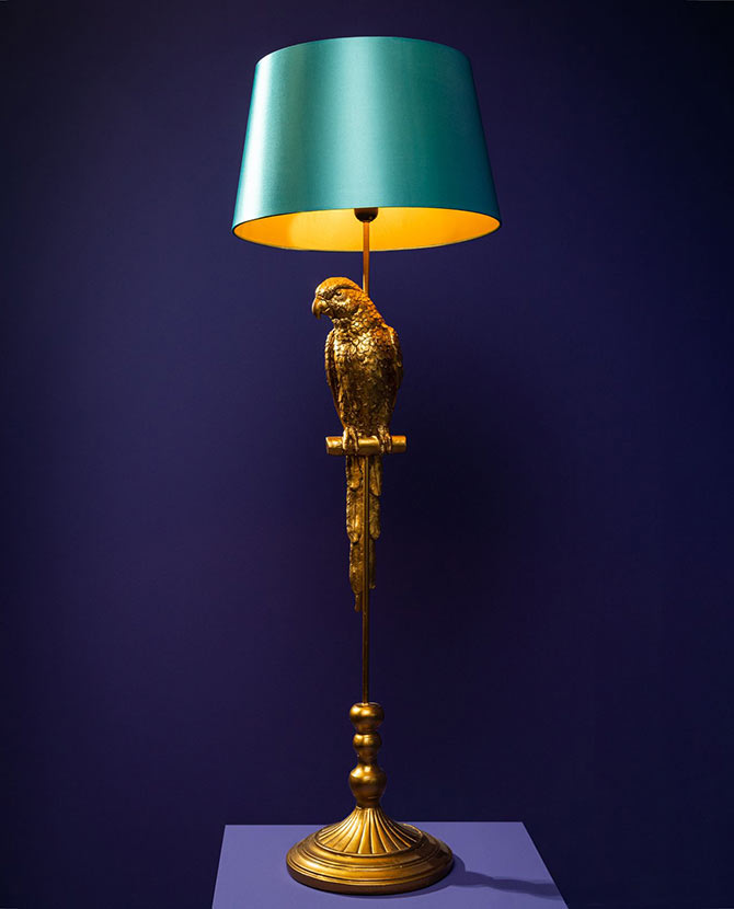 Aranyszínű papagáj figurával díszített, 121 cm magas, trópusi, glamour stílusú állólámpa, türkizszínű lámpaernyővel , kék színű háttér előtt.