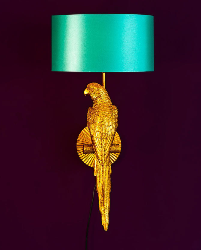 Aranyszínű papagáj figurával díszített, trópusi, glamour stílusú falilámpa, türkizszínű lámpaernyővel., lila háttér előtt.