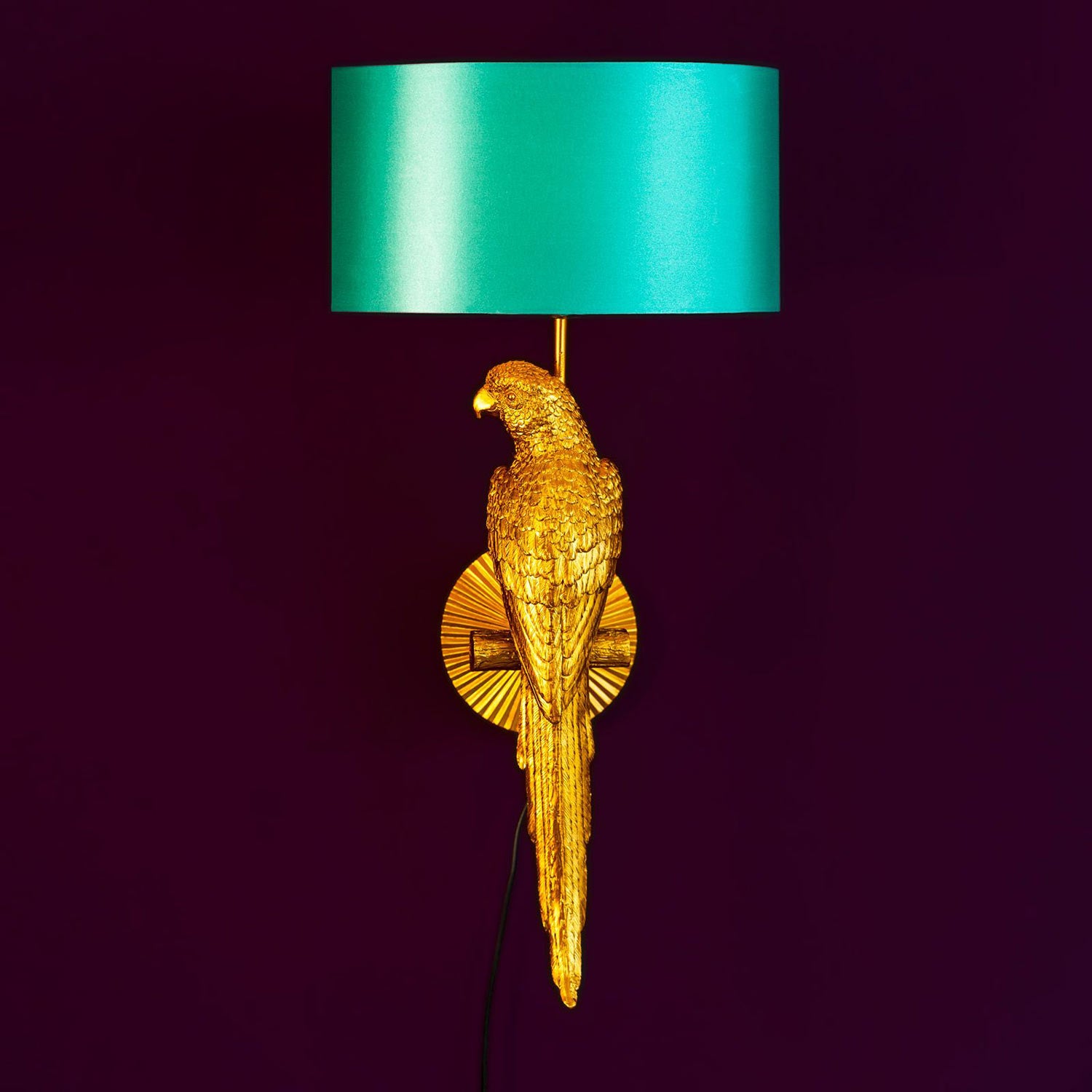 Aranyszínű papagáj figurával díszített, trópusi, glamour stílusú falilámpa, türkizszínű lámpaernyővel., lila háttér előtt.