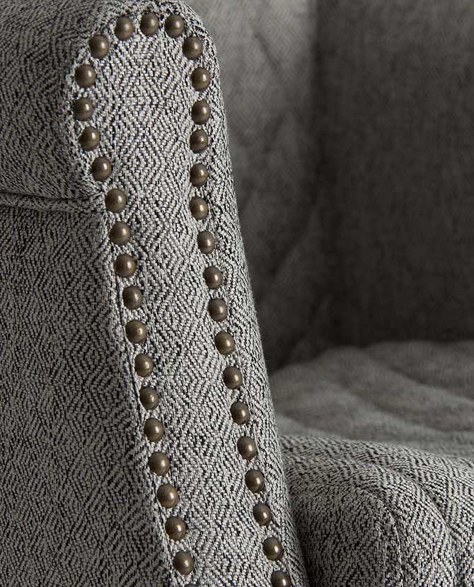 Skandináv stílusú, szürke szövettel kárpitozott modern fotel réz szegecsei.