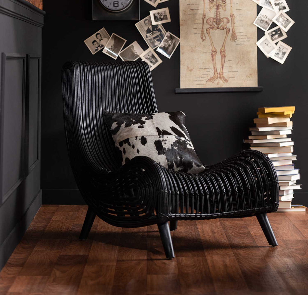 Fekete színű rattan pihenő fotel fekete színű fal előtt könyvekkel.