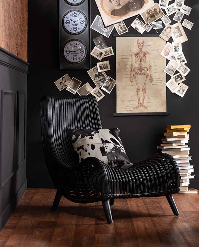Fekete színű rattan pihenő fotel fekete színű fal előtt könyvekkel. 