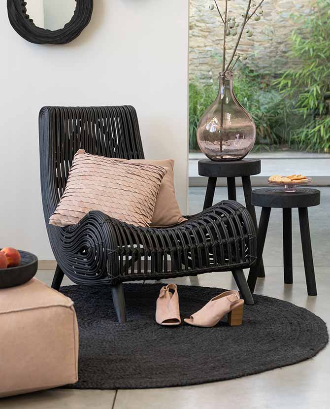 Fekete színű rattan pihenő fotel teraszon, bézs párnákkal, női cipővel és vázával. 