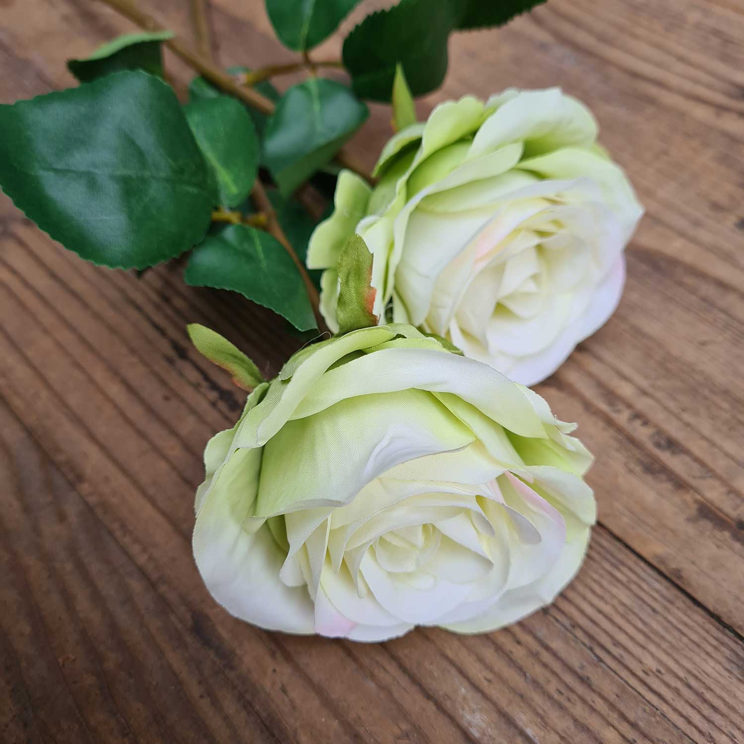 Világoszöld színű mű rózsák natúr színű fa asztalon.