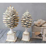 Kétféle méretű, antikolt krémszínű, fém toboz dísz szürke fal előtt, karácsonyi ajándékokkal.