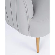 Skandináv stílusú, halványszürke színű bársonnyal kárpitozott fotel, aranyszínű fém lábak részlete.