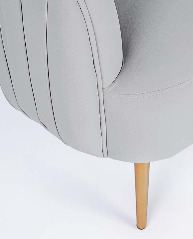 Skandináv stílusú, halványszürke színű bársonnyal kárpitozott fotel, aranyszínű fém lábak részlete.