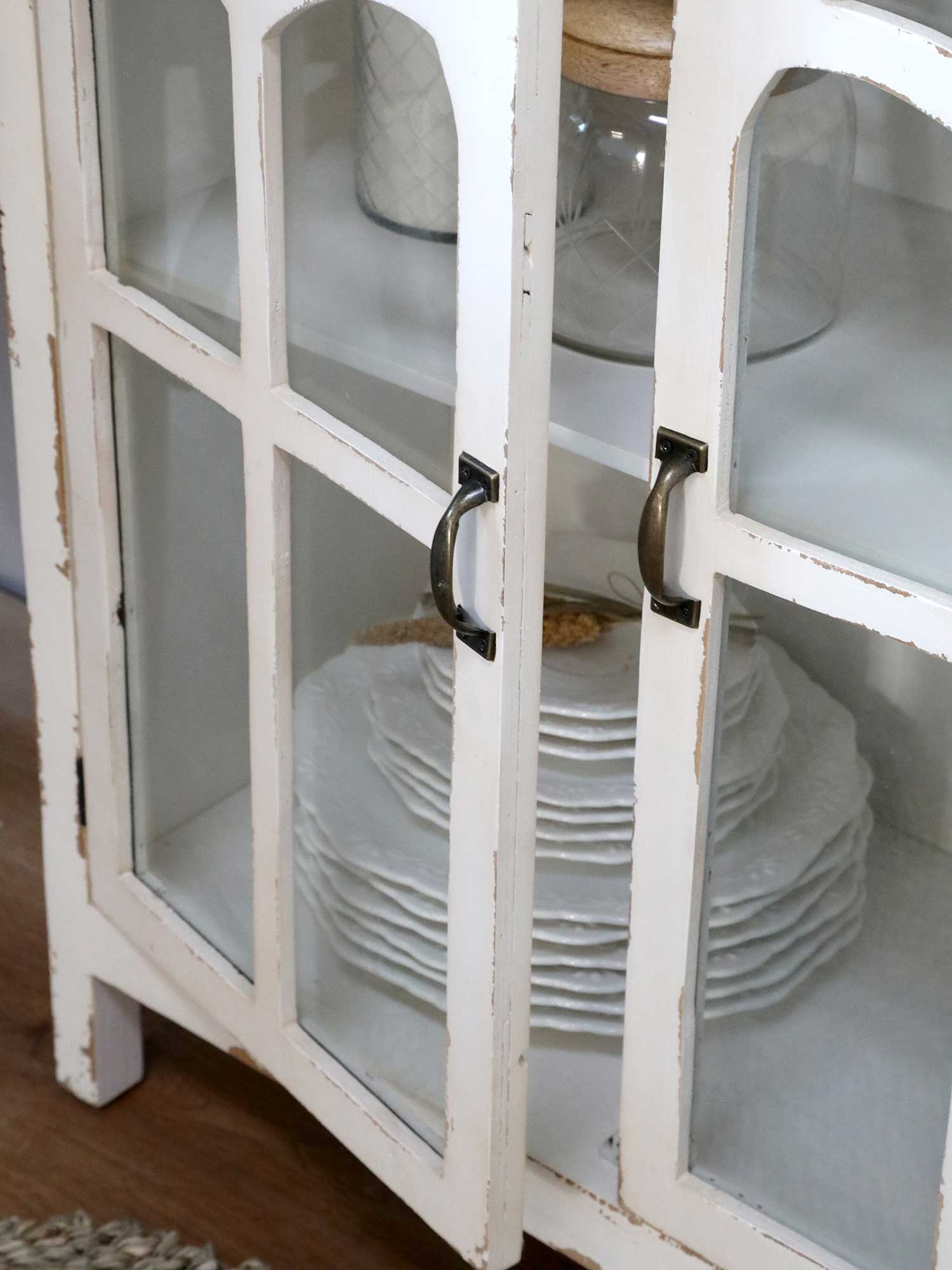 Antik krém színű vitrines tárolószekrény nyitott ajtaja, bronz színű fogantyúkkal.