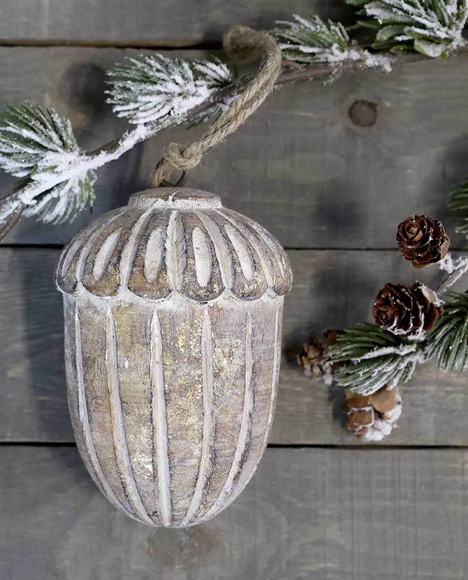 Vintage stílusú, mangófából faragott, 15 cm magas, antikolt felületű, tölgy makk formájú, kézműves karácsonyfadísz szürke deszkaasztalon havas fenyővel 