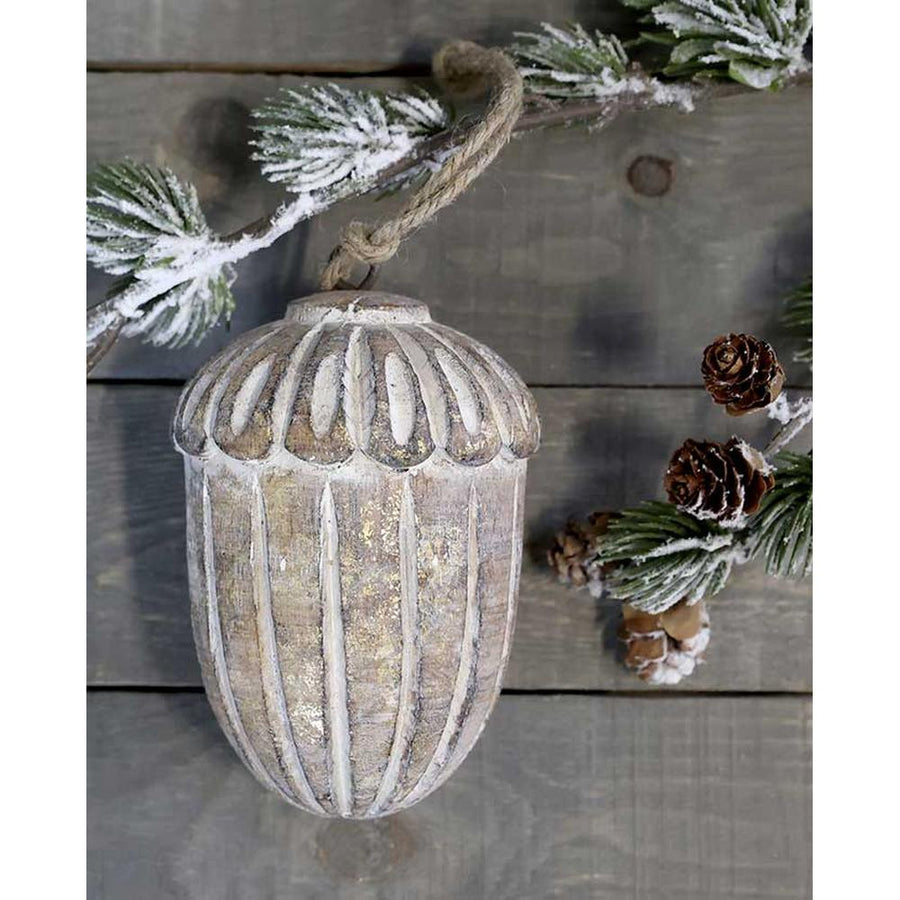 Vintage stílusú, mangófából faragott, 15 cm magas, antikolt felületű, tölgy makk formájú, kézműves karácsonyfadísz szürke deszkaasztalon havas fenyővel 