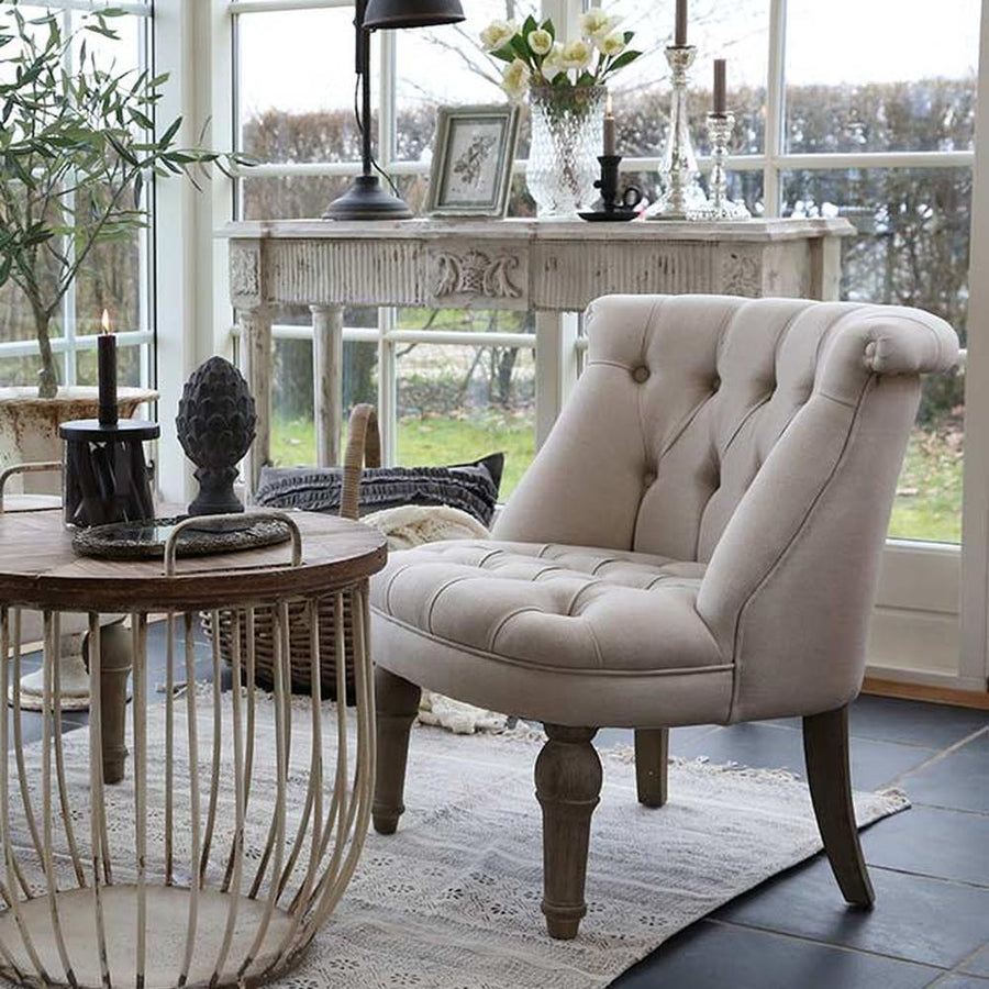 Francia stílusú vintage fotel masszív tölgyfa lábakkal, ekrü színű, gombbehúzásos technikával díszített tűzálló pamutvászon kárpittal nagy üvegablakos nappaliban loft stílusú dohányzóasztallal 