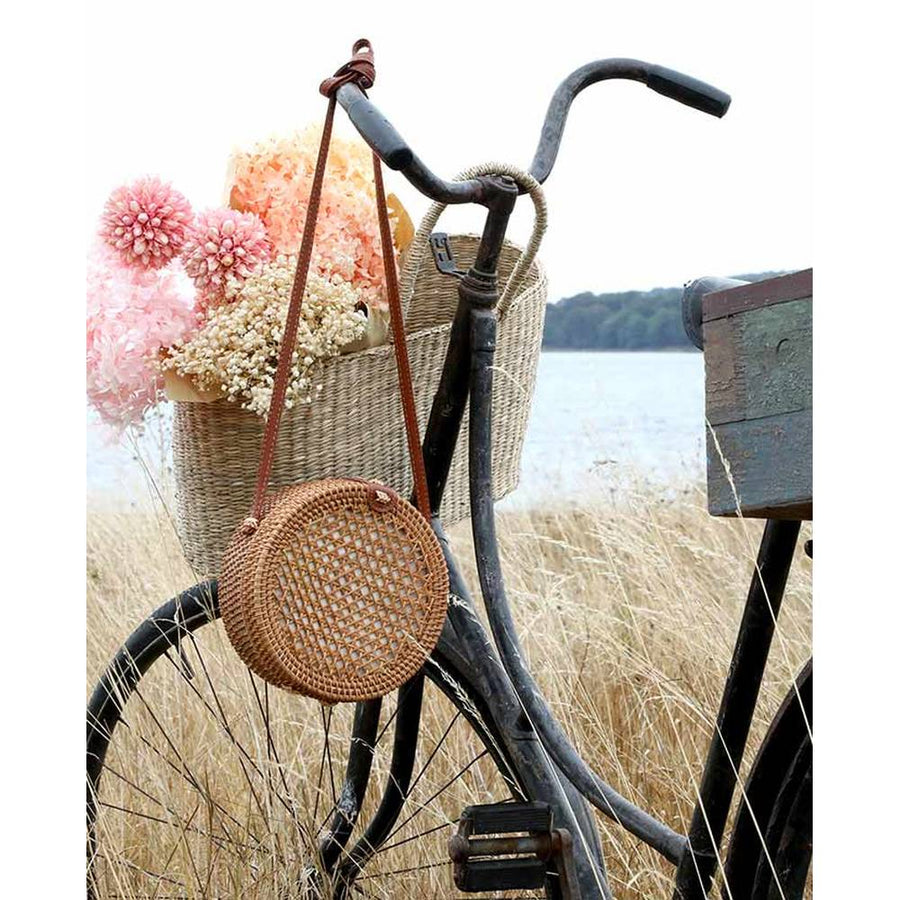 Vintage stílusú, autentikus, kör formájú, növényi rattanból és bőrből készült kézműves női táska vintage kerékpáron a mezőn 