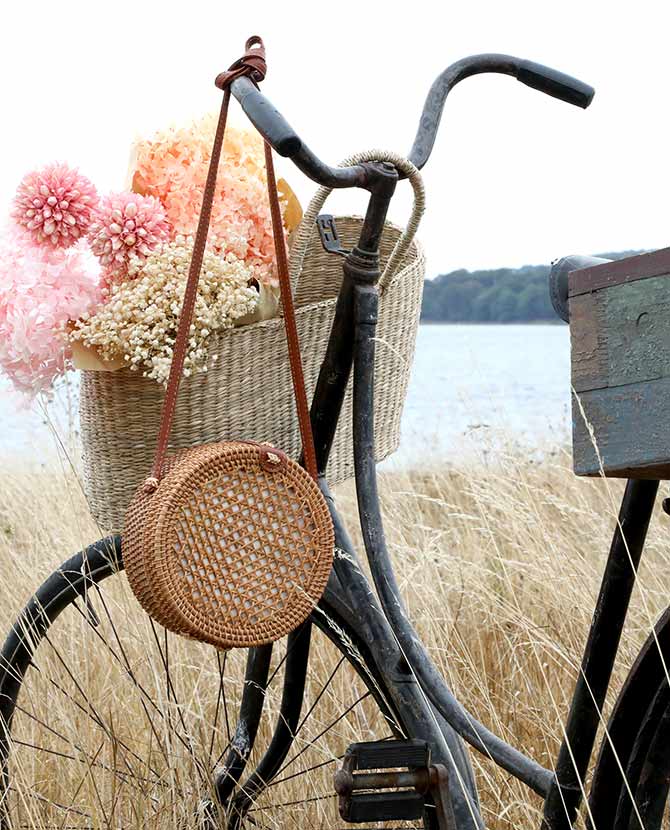 Vintage stílusú, autentikus, kör formájú, növényi rattanból és bőrből készült kézműves női táska vintage kerékpáron a mezőn 