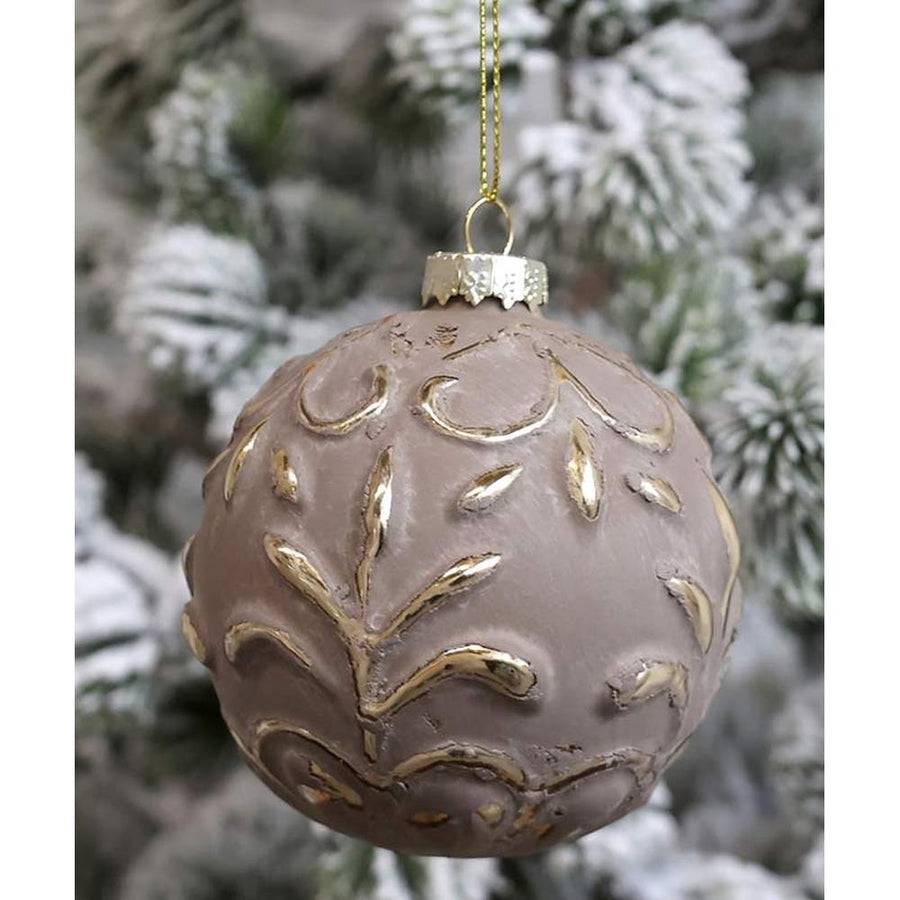 Vintage stílusú, aranyszínű növényi dombormintával díszített, gömb formájú, mokkaszínű üveg karácsonyfadísz, havas fenyőfán.