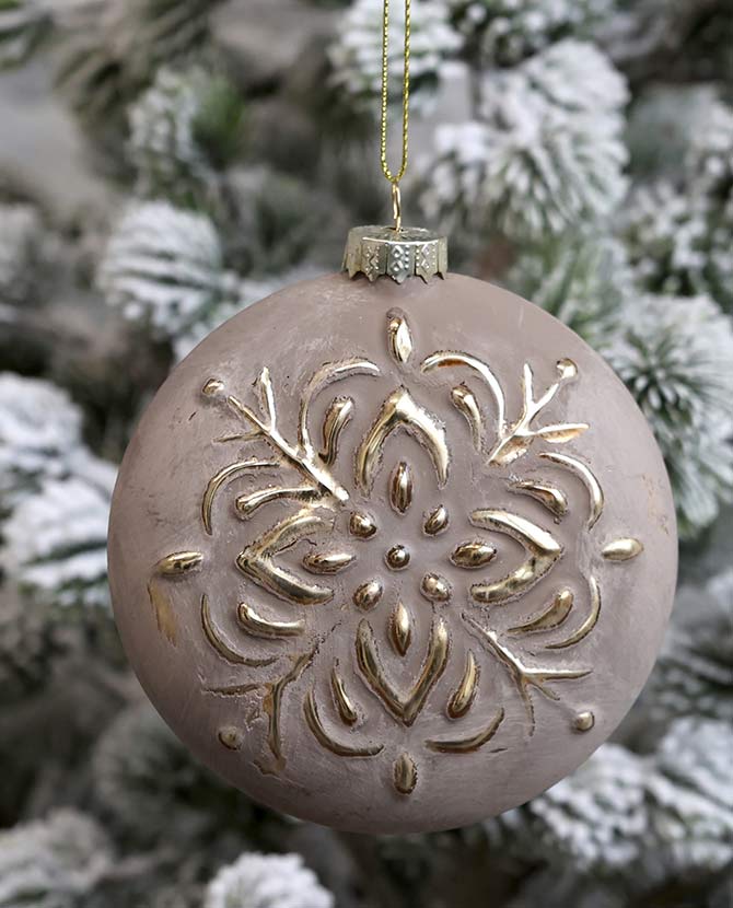 Vintage stílusú, aranyszínű növényi dombormintával díszített, gömb formájú, mokkaszínű üveg karácsonyfadísz, havas fenyőfán.