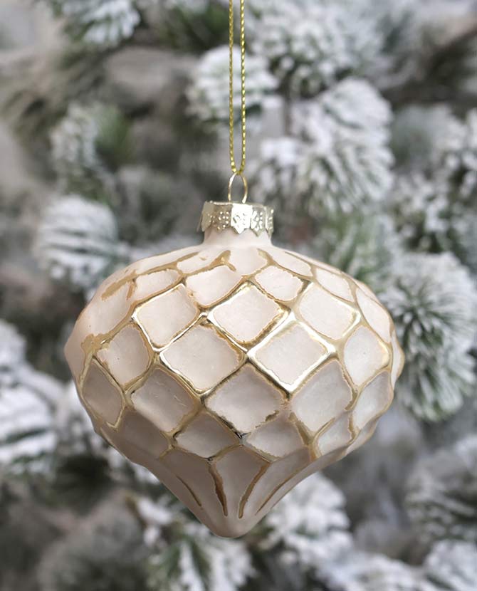 Vintage stílusú, aranyszegélyes rombusz alakú dombormintával díszített, csepp formájú, púderszínű üveg karácsonyfadísz., havas fenyőfán.